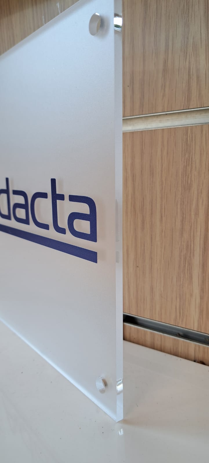 Targa in plexiglass satinato con logo blu stampato, fissata a parete con distanziatori